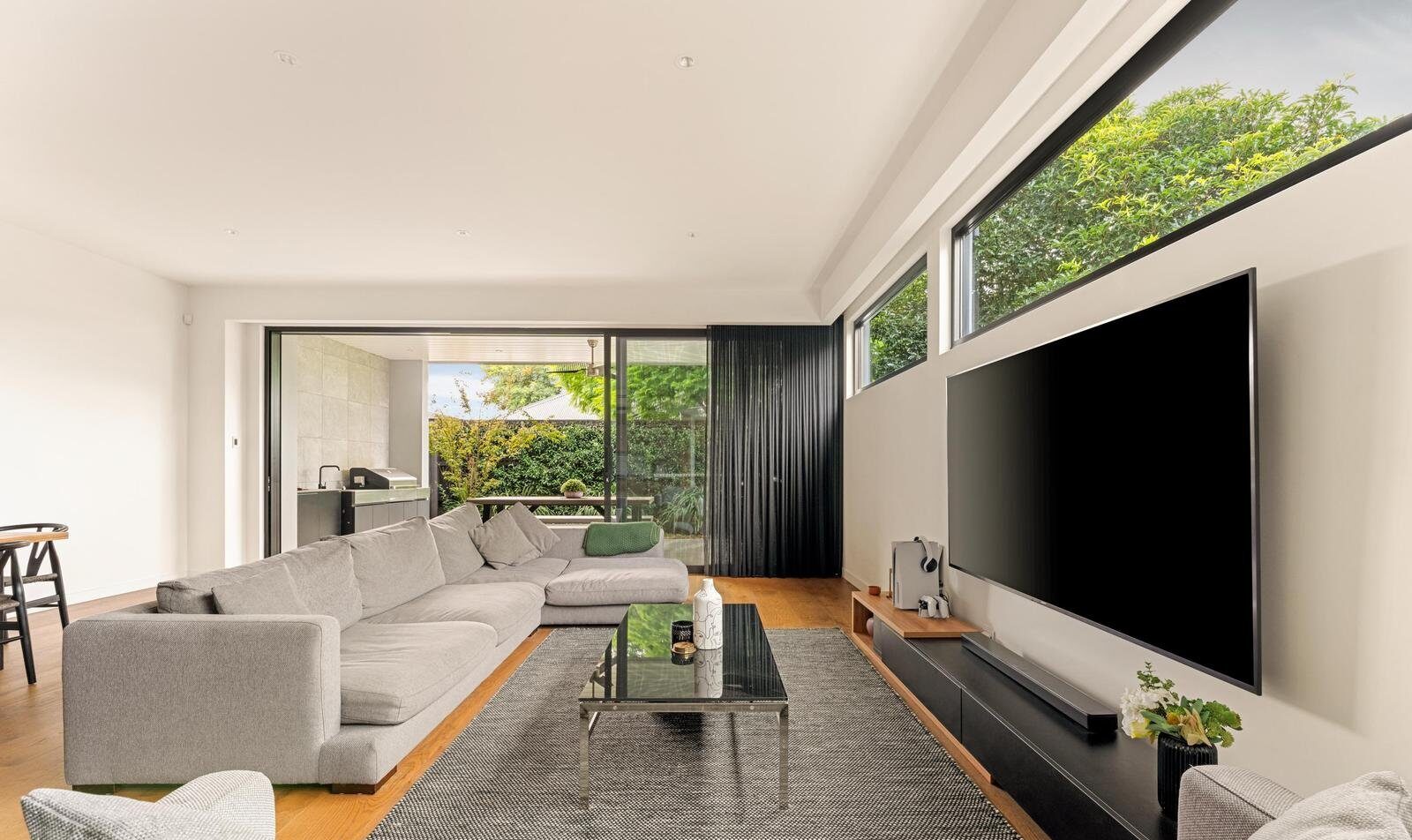 5 eden street cheltenham ;ooking over the lounge room with two couches, large tv, with the sliding doors open aloowing you to see through to the backyard